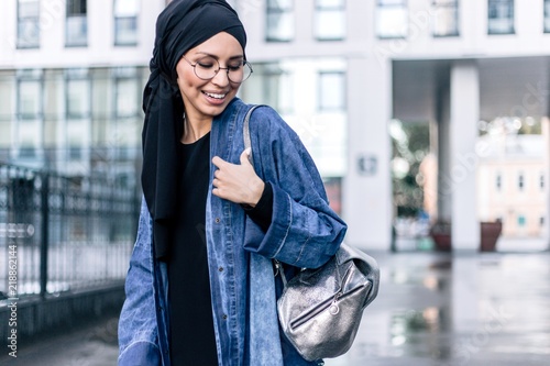 Stylish Muslim girl hijab stands among the city with a women's bag