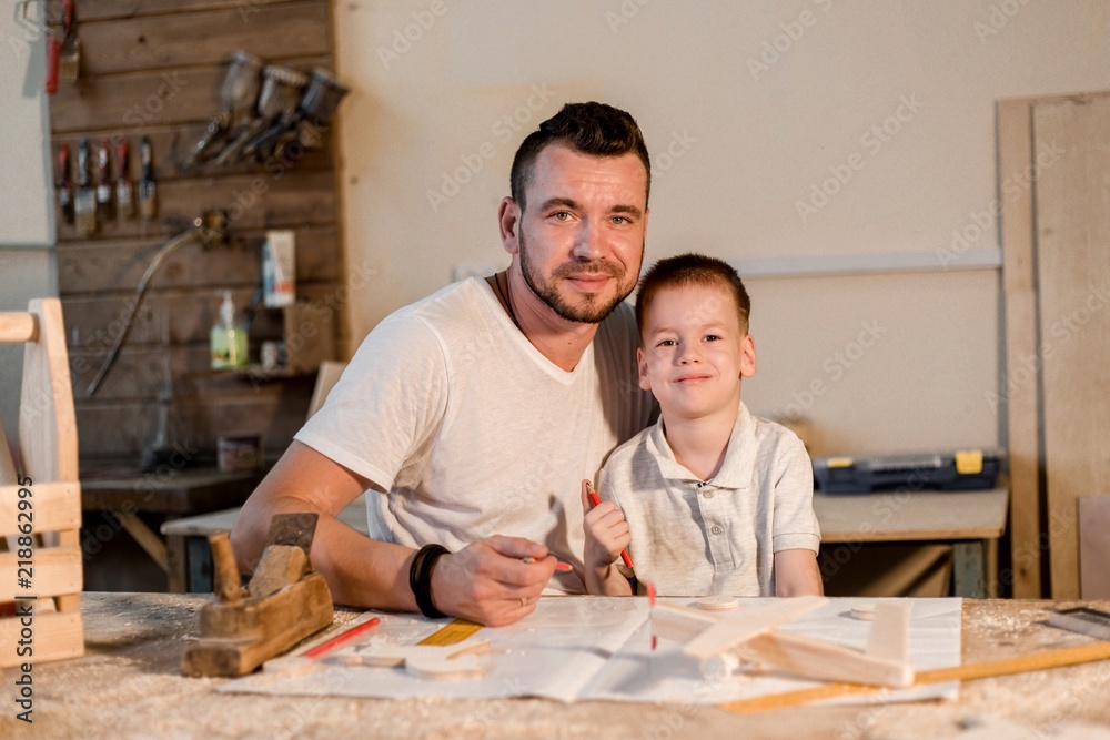 Father and son in the workshop playing are designing a model of the future wooden toys Father and son in the workshop playing are designing a model of the future wooden toys