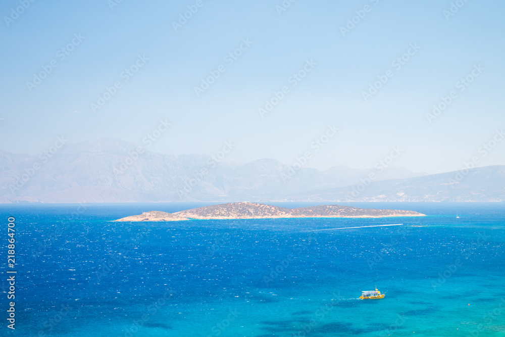 Agii Pantes Agios Nikolaos,Crete, Greece. Small uninhabited island near to Agios Nikolaos and Elounda. Blue sea and boat at summer. Agii Pantes Agios Nikolaos,Crete, Greece. Small uninhabited island near to Agios Nikolaos and Elounda. Blue sea and boat at summer.