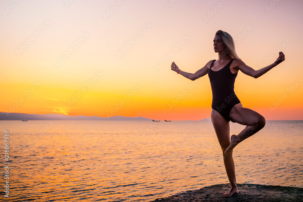 Silhouette of a girl doing yoga on the pier by the sea, standing asana Vrikshasana at sunrise. Healthy lifestyle.