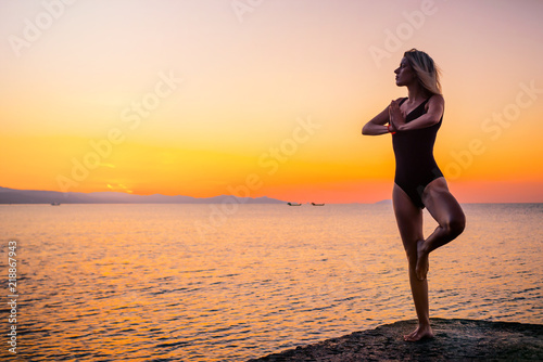 Beautiful girl in black doing yoga on the pier by the sea, standing asana Vrikshasana at sunrise. Healthy lifestyle. © indigo_nifght