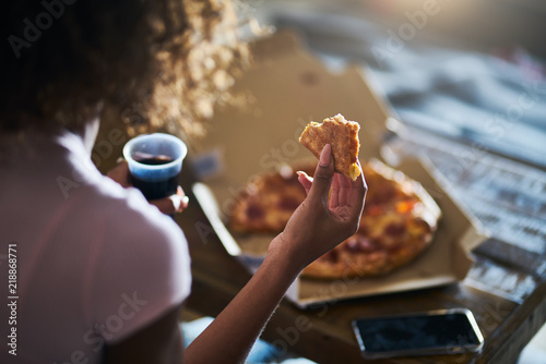 woman eating pizza and drinking cola while sitting on sofa watching tv in home late at night photo