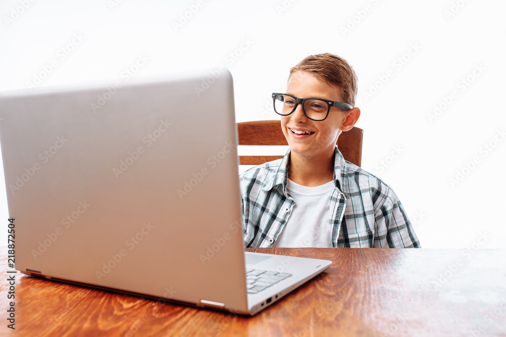 A young man resting after school sitting at the table and watching a movie on a laptop, throwing his hands behind his head, on a white background, in the Studio A young man resting after school sitting at the table and watching a movie on a laptop, throwing his hands behind his head, on a white background, in the Studio