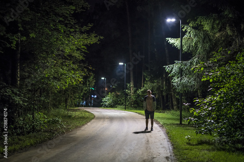 alone young man in casual walking on the night forest road with the street lights