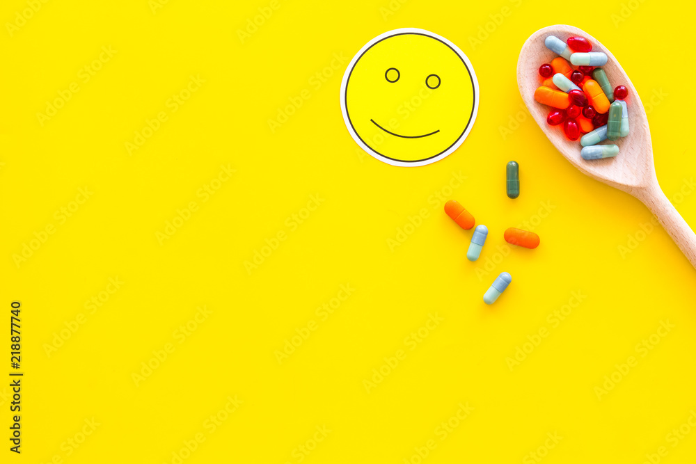 Fototapeta premium Reception of medicines concept. Recovery. Pills in spoon near smile face emoji on yellow background top view copy space