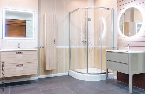 Spacious and bright modern bathroom interior with white walls, a shower cabin with glass wall, a toilet and faucet sink