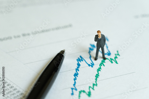 Business company profit, investment and financial report analysis concept, miniature people figurine success businessman standing reviewing stock exchange or yearly revenue graph data report