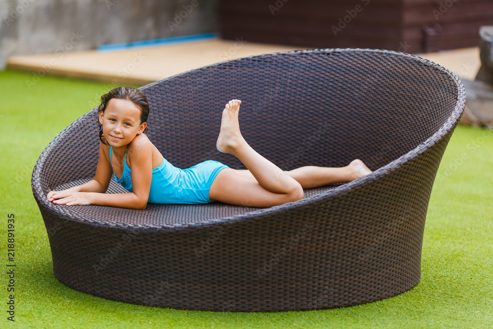 Charming girl 8 years old sunbathing on a wicker sofa in the courtyard of  the hotel Stock Photo | Adobe Stock