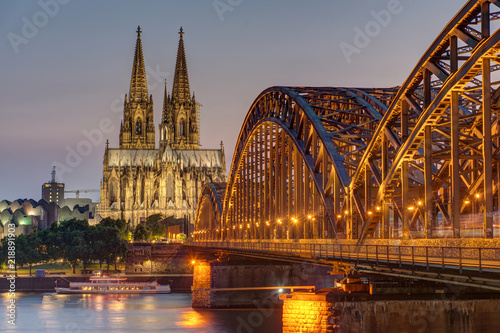 The imposing cathedral of Cologne with the Hohenzollern bridge over the river Rhine at dusk