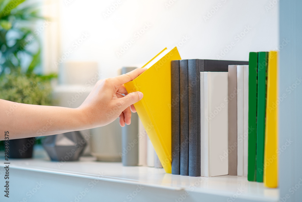 Naklejka premium Male hand choosing and picking white book on white bookshelf in public library, education research and self learning in university life concepts