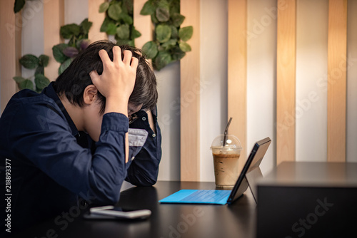 Young Asian businessman feeling stressed and frustrated while working with digital tablet in coffee shop. Business problem concept
