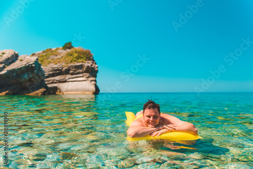 young man at yellow inflatable mattress in clear transparent water