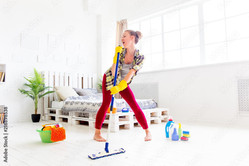 Woman in protective gloves is smiling and wiping dust using a spray and a duster Woman in protective gloves is smiling and wiping dust using a spray and a duster