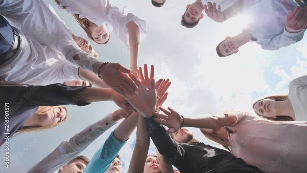 Students graduates gather around and lay their hands in a sign of successful work.