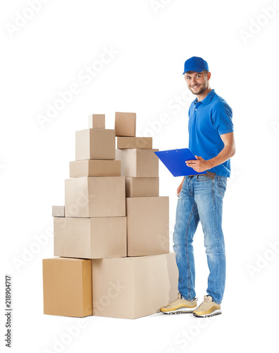 Full length portrait of courier fills paper near stack of parcels boxes