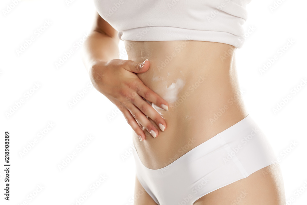 Young woman applying cream on her belly on white background