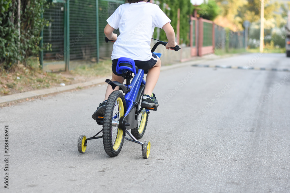 Five years old boy rides a bicycle down the street. Child riding bicycle outdoor.