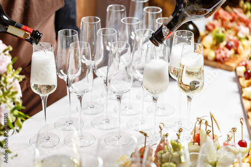Bartender pouring champagne or wine into wine glasses on the table in restaurant. solemn wedding ceremony or happy new year banquet