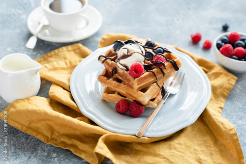 Belgian waffles with vanilla ice cream and berries drizzled with chocolate and cup of coffee on the background. Selective focus