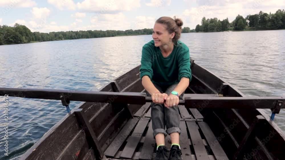 A young beautiful woman is sailing on a boat on the lake. A strong woman paddles with oars. A young beautiful woman is sailing on a boat on the lake. A strong woman paddles with oars.