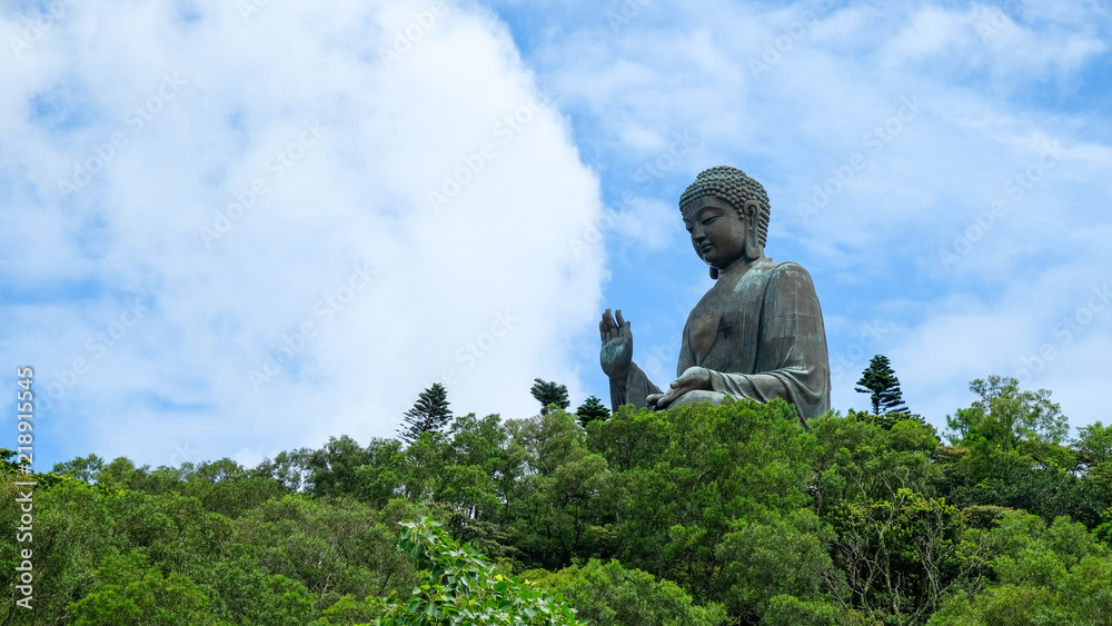 Fototapeta premium Tian Tan Buddha over the forrest with blue sky background located at Ngong Ping, Lantau Island, in Hong Kong