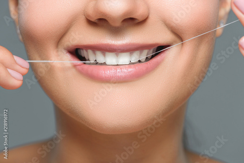 partial view of smiling woman with beautiful white teeth and dental floss isolated on grey