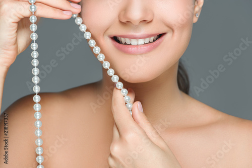 cropped shot of smiling woman with white teeth and pearls in hands isolated on grey