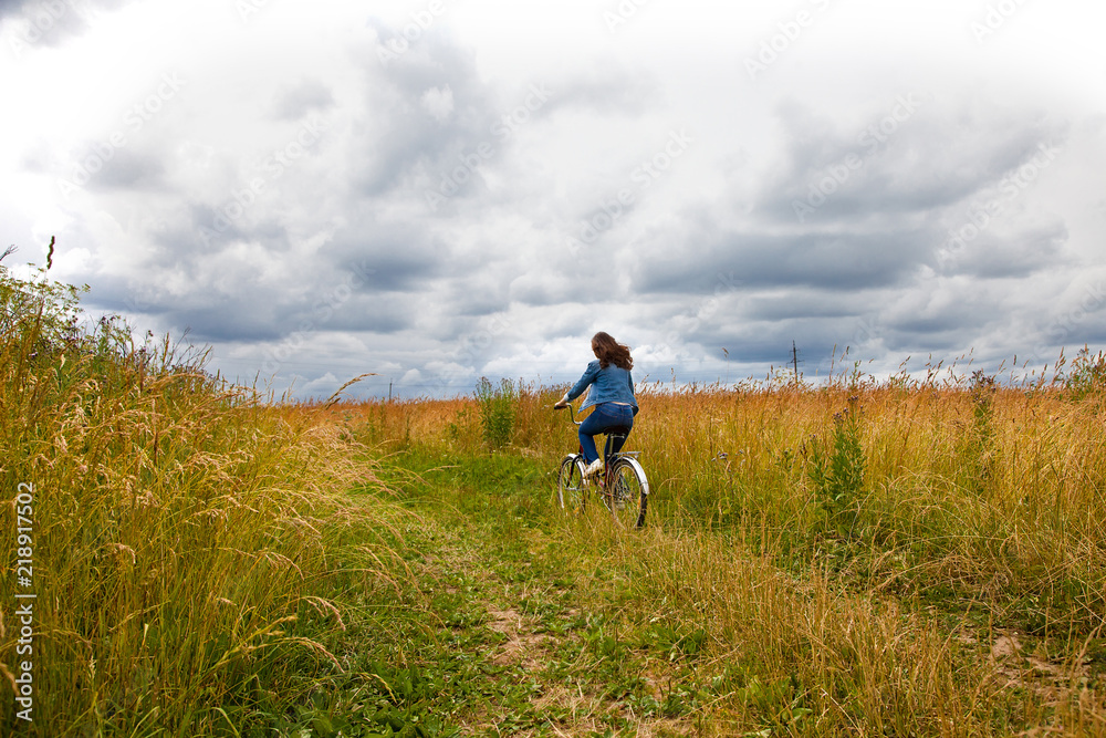 Happy Young Woman riding bicycle on a yellow field. Healthy Lifestyle.