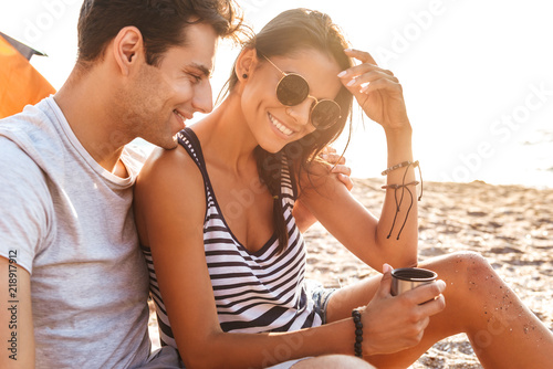 Sticker Young cute loving couple drinking tea on the beach outdoors.