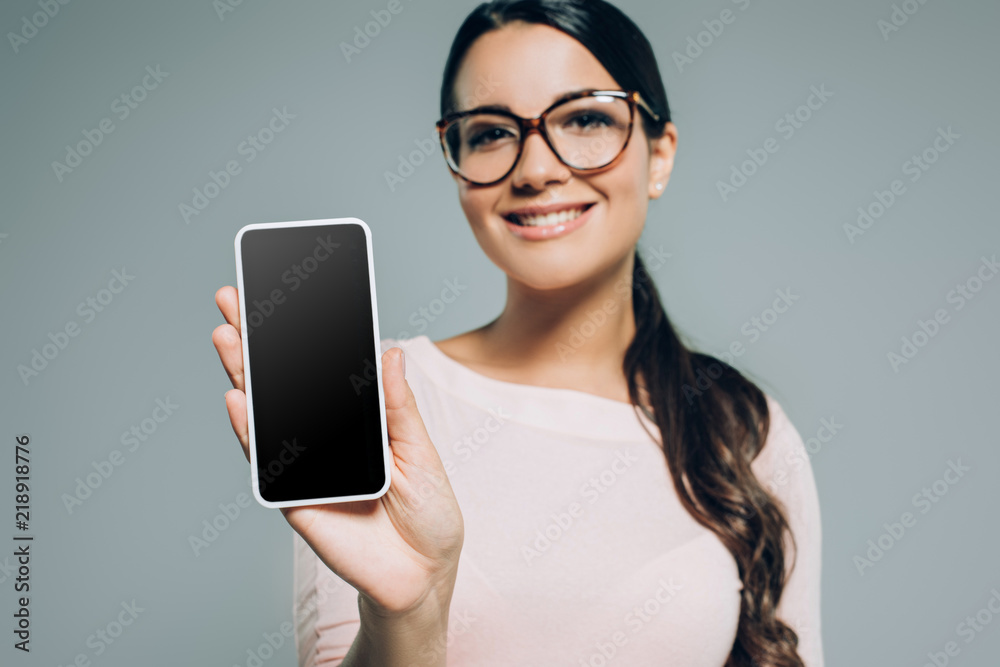 young woman showing smartphone with blank screen, isolated on grey