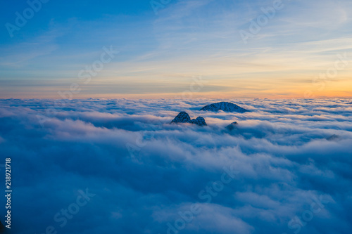 Background photo of low clouds in a mountain valley, vibrant blue and orange sky. Sunrise or sunset view of mountains and peaks peaking through clouds. Winter alpine like landscape of high Tatras.