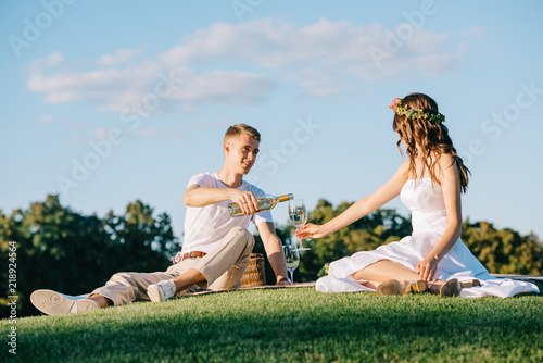 groom pouring wine into glass for bride on picnic