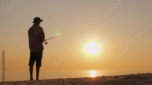 Silhouette of a young fisherman fishing on the beach at sunset