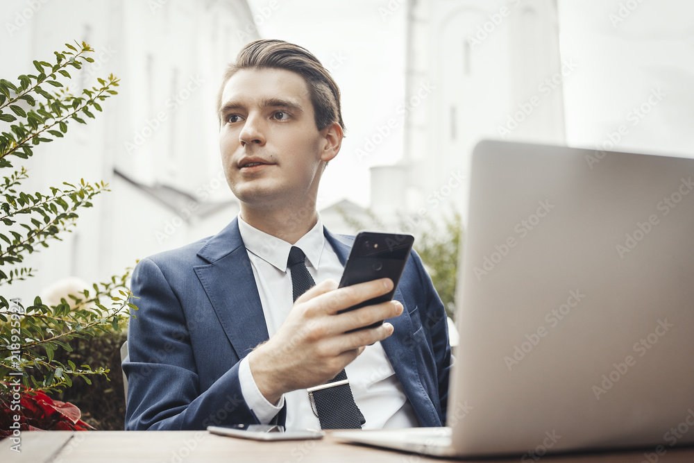 Young attractive businessman holding mobile phone in hand and looking aside. Young attractive businessman holding mobile phone in hand and looking aside.
