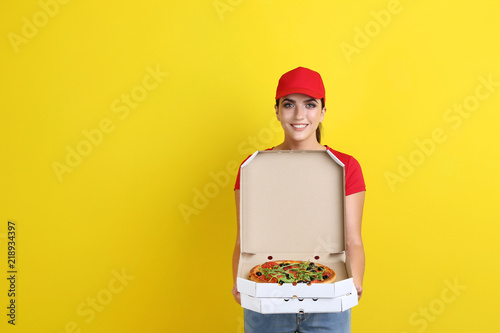 Delivery woman with pizza in cardboard box on yellow background