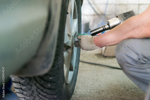 Auto mechanic man with electric screwdriver changing tire outside. Car service. Hands replace tires on wheels. Tire installation concept.