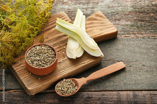 Ripe fennel bulbs and dry seeds in bowl and spoon on wooden table