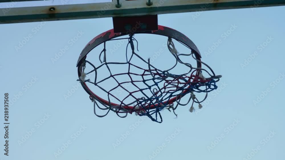 Throwing ball into basketball ring against blue sky, through hoop, outdoors Throwing ball into basketball ring against blue sky, through hoop, outdoors