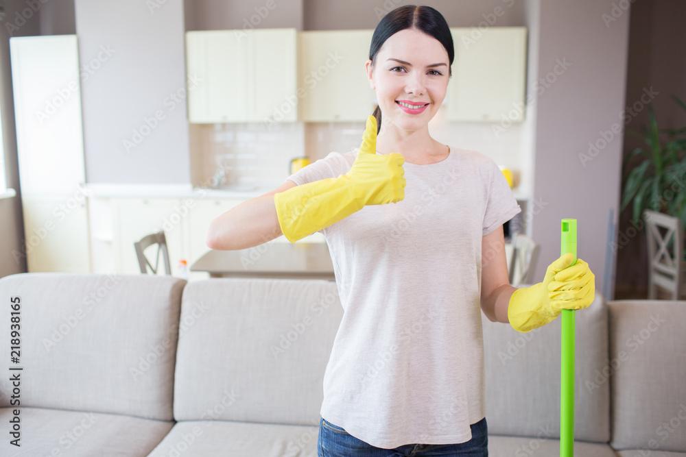 Girl stands in apartment and shows her big thumb up. Woman wears yellow gloves and hold green stick with left hand. She is positive. Girl stands in apartment and shows her big thumb up. Woman wears yellow gloves and hold green stick with left hand. She is positive.