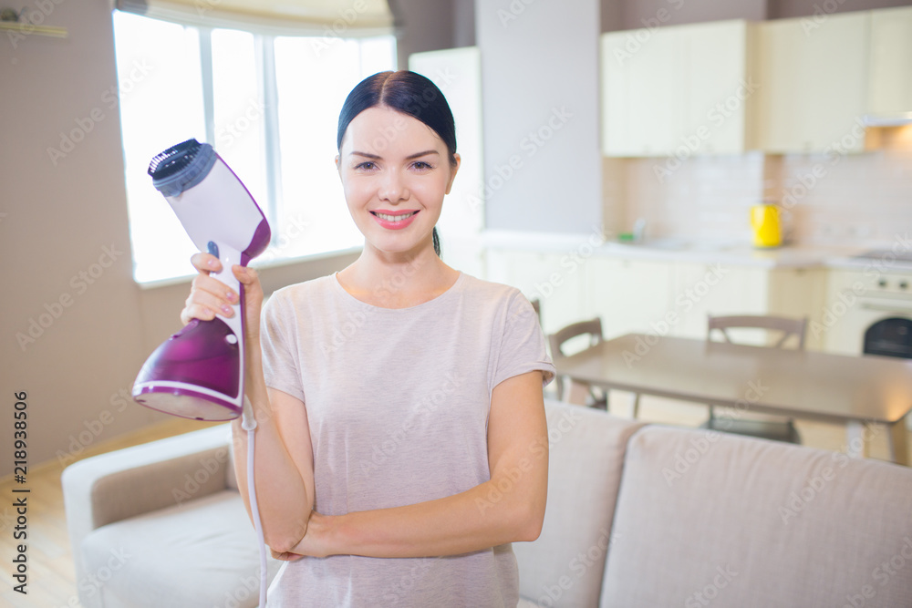 Pretty woman stands with small vacuum cleaner in hand and poses on camera. She has finishes cleaning. Girl looks happy. Pretty woman stands with small vacuum cleaner in hand and poses on camera. She has finishes cleaning. Girl looks happy.
