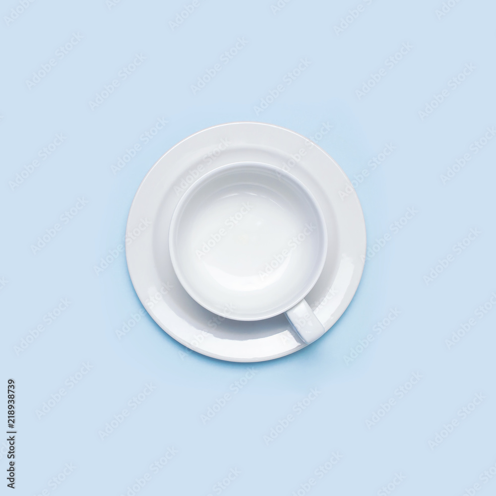 Flat lay top view White empty ceramic cup on a saucer on blue background. Concept morning breakfast, drink coffee or tea. Background utensils, kitchen items. Minimalistic background Flat lay top view White empty ceramic cup on a saucer on blue background. Concept morning breakfast, drink coffee or tea. Background utensils, kitchen items. Minimalistic background