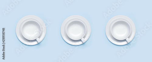 Flat lay top view three White empty ceramic cup on a saucer on blue background. Concept morning breakfast, drink coffee or tea. Background utensils, kitchen items. Minimalistic background