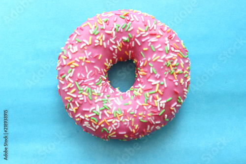 Donut in pink glaze and colored sprinkles isolated on a blue background, top view