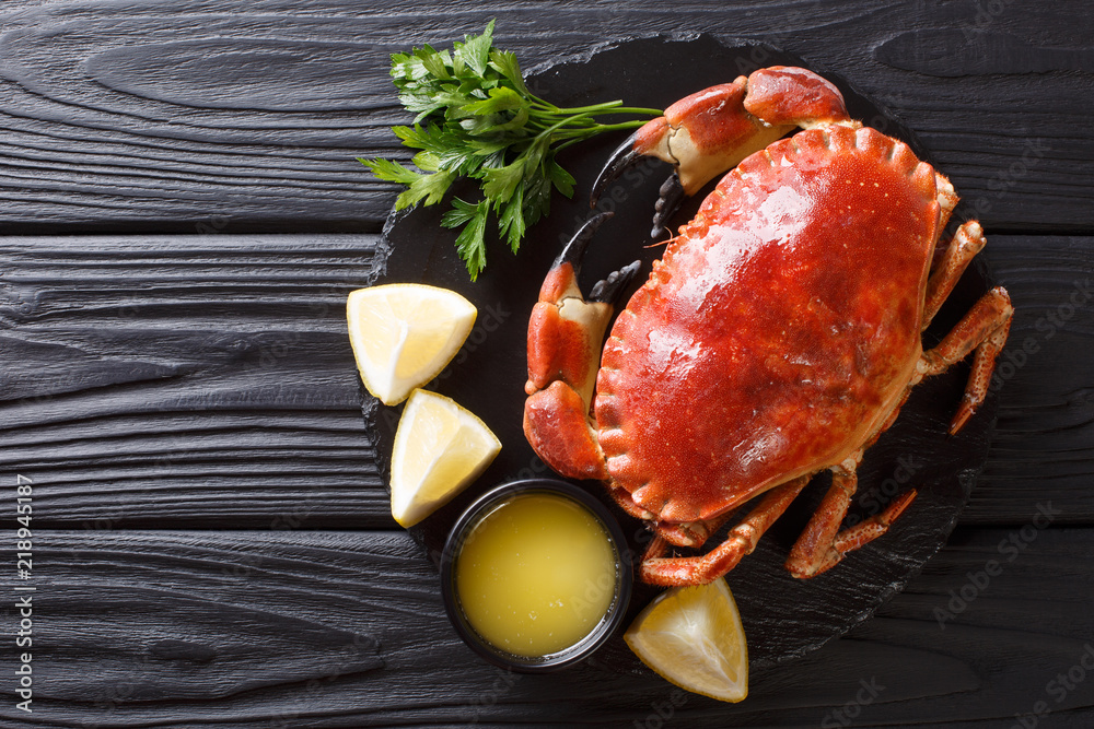 Delicious traditional boiled whole brown crab with sauce, lemon and parsley on a slate board close-up. Horizontal top view Delicious traditional boiled whole brown crab with sauce, lemon and parsley on a slate board close-up. Horizontal top view