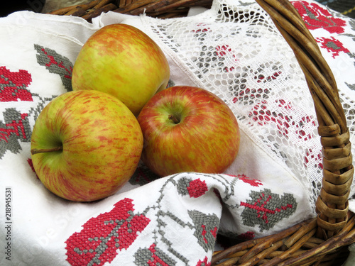 Wicker basket with fresh apples on fabric with embroidered patterns. Concept for autumn harvest or needlework, rural background