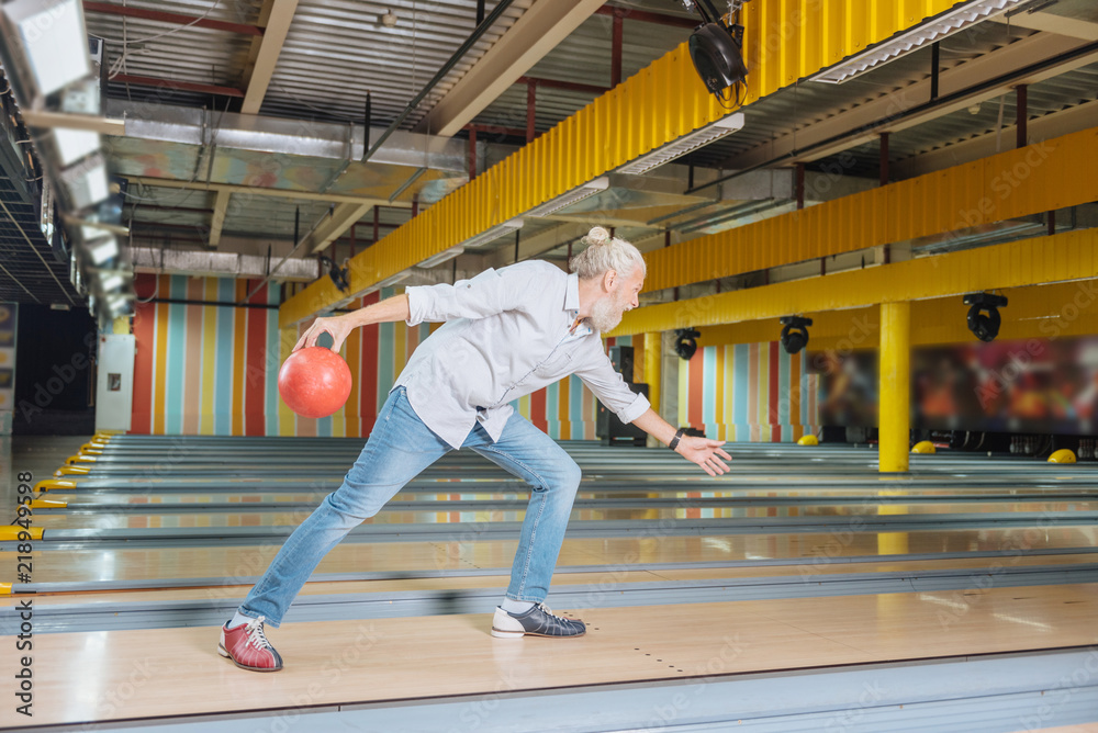 Obraz premium Favourite entertainment. Nice aged man holding a bowling ball while enjoying the game