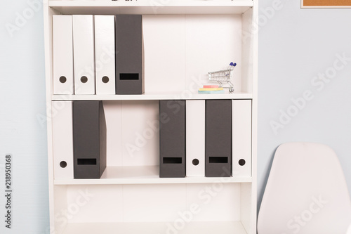 Interior, office concept - a white shelf with an amount of files and small toy grocery trolley