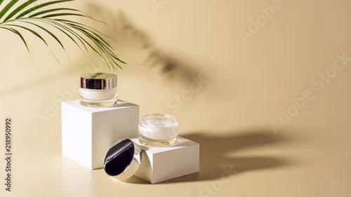 Obraz close up view of palm leaf, facial and body creams in glass jars on white cubes on beige background