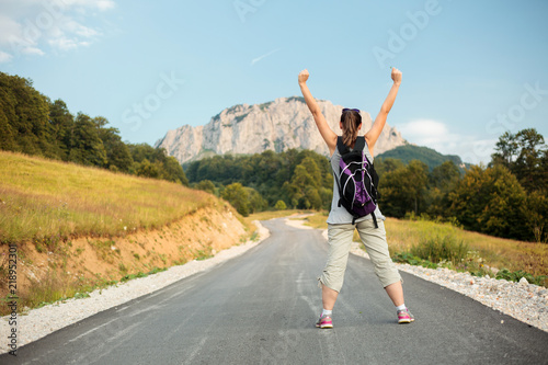 Young woman standing with arms raised in the air and enjoying the view of the surrounding peaks. Tranquility in nature.