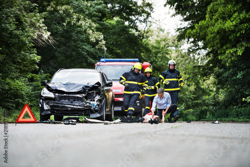 Firefighters running to rescue a woman lying unconscious on the road after a car accident.